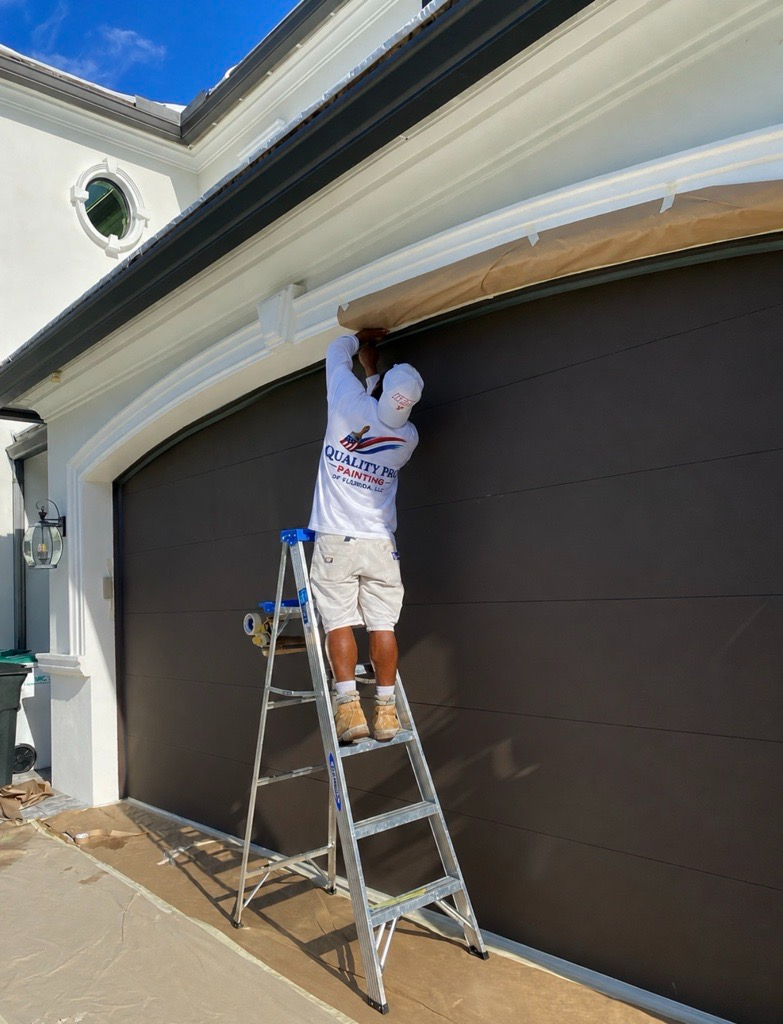 Quality Pro Painting crew member masking trim above a garage door